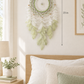 Handcrafted olive green angel dream catcher above a bed in a light bedroom, 13 x 23 inches